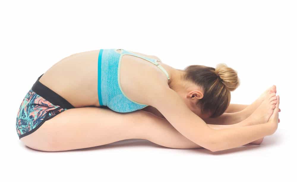 Sporty beautiful young female doing yoga seated forward bend / Paschimottanasana isolated on white background.