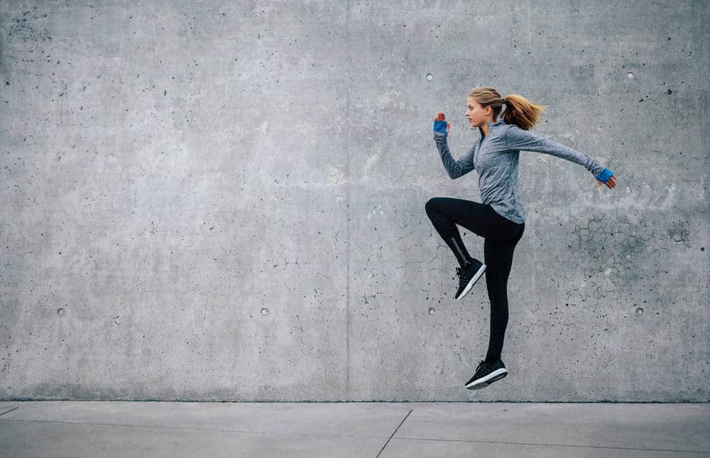 Side view shot of fit young woman doing cardio interval training against grey background.